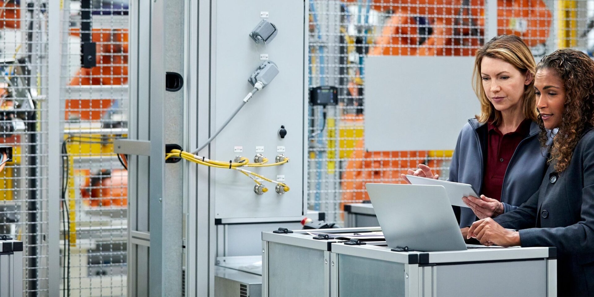 Image of two women collaborating on a computer and tablet in a factory.