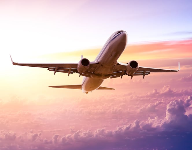 Image of a commercial airline ascending above the clouds at sunset.