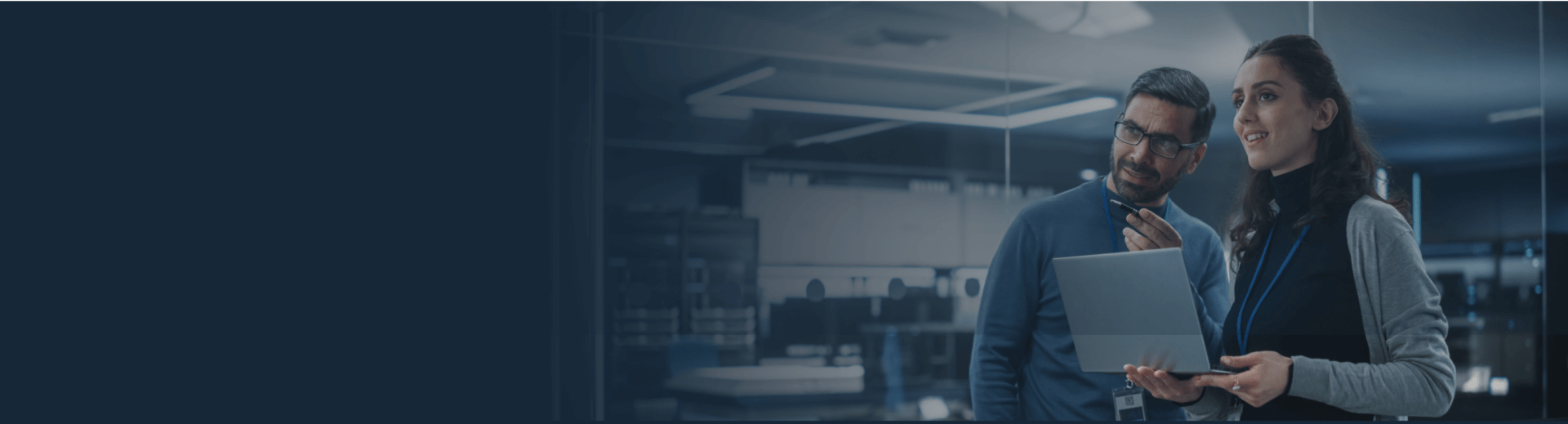 Two coworkers discussing automated software testing inside building holding laptop